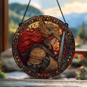 May include: Round stained glass window art featuring a warrior with red hair, wearing gold armor and a winged helmet, holding a sword. The artwork is in a stained glass style with a black chain for hanging.