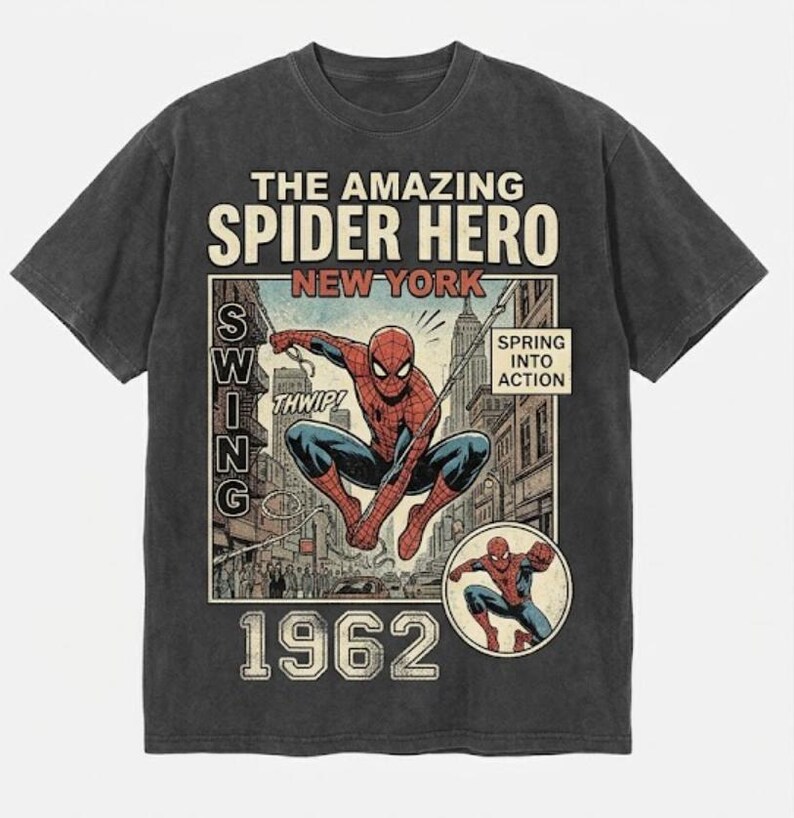 Pode incluir: T-shirt cinzenta escura com um gr&aacute;fico em estilo de banda desenhada vintage do Homem-Aranha. O design inclui o texto "THE AMAZING SPIDER HERO NEW YORK 1962" e "SPRING INTO ACTION". Uma imagem menor do Homem-Aranha est&aacute; no canto inferior direito.