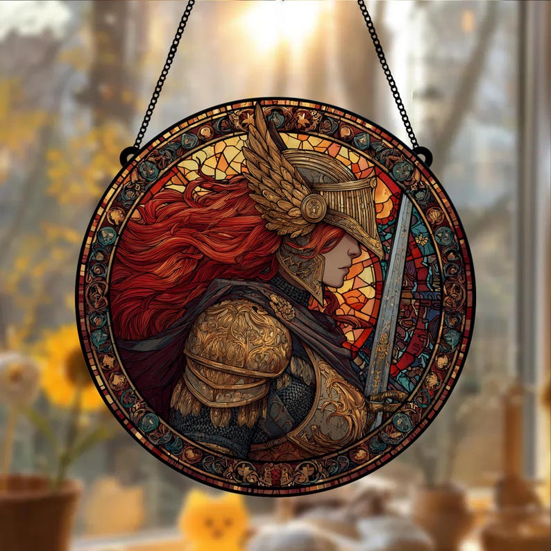 May include: Round stained glass window art featuring a warrior with red hair, wearing gold armor and a winged helmet, holding a sword. The artwork is framed with a black border and a chain for hanging. The background is a colorful mosaic.
