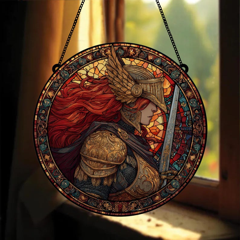 May include: Round stained glass window art featuring a warrior with red hair, wearing gold armor and a helmet with wings. The warrior holds a sword. The artwork is framed with a black border and hangs from a chain.