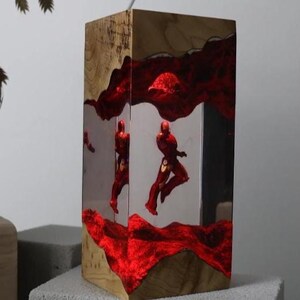 Puede incluir: L&aacute;mpara rectangular de madera con interior de resina transparente. La l&aacute;mpara presenta un dise&ntilde;o rojo texturizado y figuras rojas en el interior. La madera tiene un patr&oacute;n de vetas natural. La l&aacute;mpara se ilumina desde dentro.