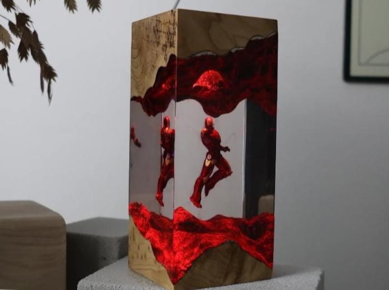 Puede incluir: L&aacute;mpara rectangular de madera con interior de resina transparente. La l&aacute;mpara presenta un dise&ntilde;o rojo texturizado y figuras rojas en el interior. La madera tiene un patr&oacute;n de vetas natural. La l&aacute;mpara se ilumina desde dentro.