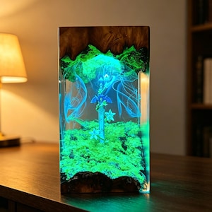 May include: A rectangular resin and wood lamp featuring a glowing green mossy base and a central sword sculpture. The interior is illuminated with bright green and blue light, creating a forest-like scene with ethereal wisps and floral accents.