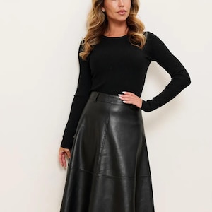 May include: A black long-sleeved ribbed knit top paired with a black knee-length A-line skirt made of a smooth material. The skirt features visible vertical and horizontal seam detailing, a structured waistband, and a flared silhouette.