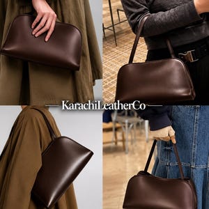 Op de afbeelding: Een donkerbruine handtas met een gladde afwerking, voorzien van een afgerond silhouet aan de bovenkant en een enkele schouderband. De tas is voorzien van de tekst KarachiLeatherCo. Het ontwerp is eenvoudig en gestructureerd met een strakke uitstraling.