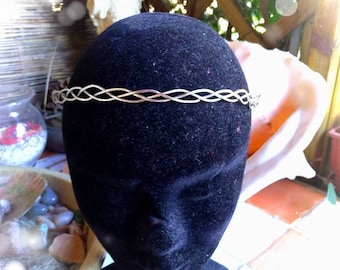 May include: A silver braided wire crown headband. The headband is on a black mannequin head.