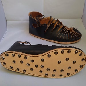 May include: A pair of black leather sandals with a brown leather sole. The sandals have a lace-up design and are decorated with metal studs.