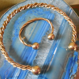 May include: Two gold-toned metal bracelets with round ball accents. The bracelets are on a blue and white agate background.
