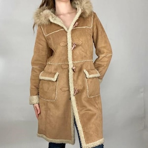 May include: A tan suede-effect coat with a faux fur-lined hood and trim. The coat has toggle fastenings, patch pockets, and a cream-coloured lining. The long coat is a vintage style.