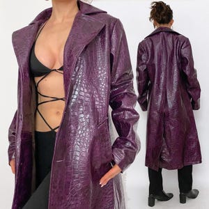 Peut inclure: Long manteau en similicuir violet avec une texture peau de crocodile. Le manteau a un col à revers classique et une fermeture à bouton. Le manteau est présenté sur une personne de face et de dos.