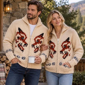 May include: Two beige knit zip-up sweaters featuring a repeating fox head pattern in red, black, and white. Each sweater has a high collar, long sleeves, and two front pockets. The knit design includes small paw print motifs near the cuffs.
