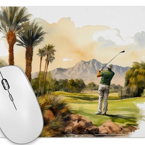 May include: Watercolor-style mousepad featuring a golfer swinging a club on a green golf course. The background includes palm trees, mountains, and a sunset sky. The mousepad is rectangular and has a white mouse on the left.