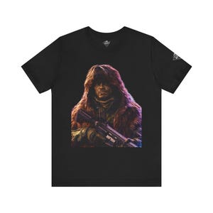 Könnte beinhalten: Schwarzes T-Shirt mit einer digitalen Illustration einer Person mit einer fellgefütterten Kapuze, die ein Gewehr hält. Das Kunstwerk hat eine dunkle, dramatische Ästhetik, wobei der Fokus auf dem Gesicht des Subjekts und der Waffe liegt. Das Shirt hat einen V-Ausschnitt und ein kleines Design am Ärmel.