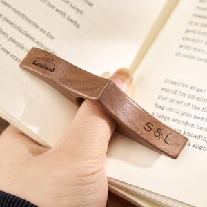 Puede incluir: Un sujetap&aacute;ginas de madera, sujeto con un dedo. El soporte marr&oacute;n oscuro tiene un icono de libro grabado y las iniciales "S & L". Este accesorio de lectura ayuda a mantener las p&aacute;ginas abiertas.