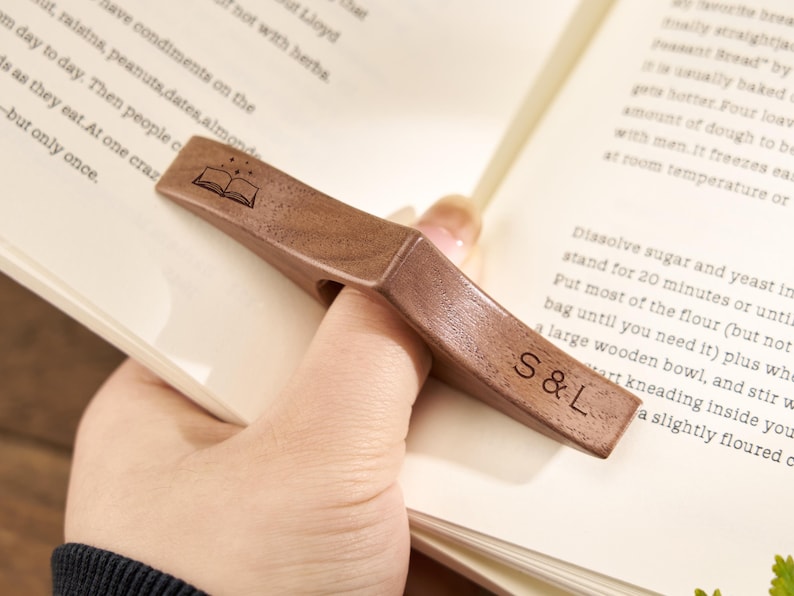 Puede incluir: Un sujetap&aacute;ginas de madera, sujeto con un dedo. El soporte marr&oacute;n oscuro tiene un icono de libro grabado y las iniciales "S & L". Este accesorio de lectura ayuda a mantener las p&aacute;ginas abiertas.