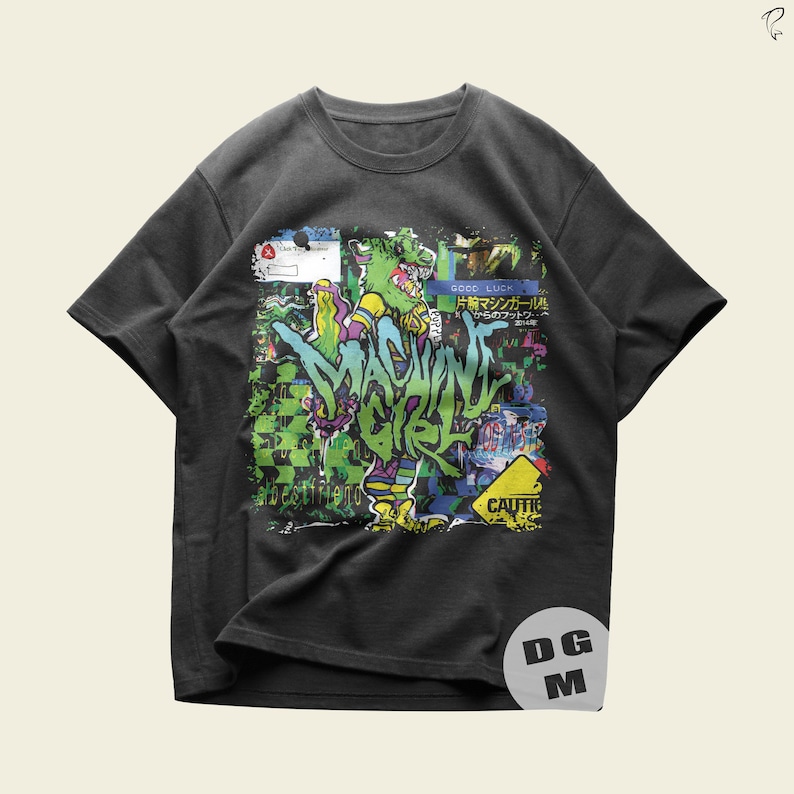 May include: A dark gray t-shirt with a colorful graphic print of a cartoon character. The graphic includes the text "MACHINE GIRL" and "GOOD LUCK".