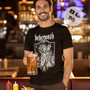 May include: A black t-shirt with a white graphic print of a woman with long hair and a crown. The graphic also includes the text "Behemoth".