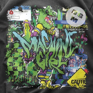 May include: A black sweatshirt with a colorful graphic print of a cartoon monster with the text "MACHINE GIRL" and "GOOD LUCK 片腕マシンガールル からのフットワ・・ 2014年" in Japanese.