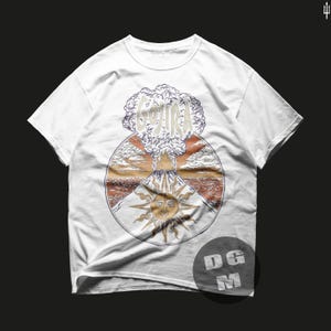 May include: White t-shirt with a graphic print of a volcano erupting with the word "GOJIRA" in the smoke cloud. The volcano is surrounded by a sun with a face and clouds. The graphic is in a circle with a brown, orange, and red background.