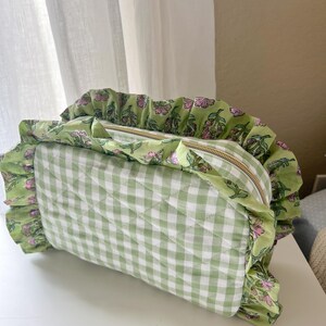 A green and white gingham-patterned bag with a ruffled trim and a zipper closure.