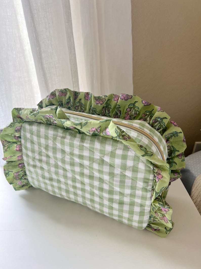 A green and white gingham-patterned bag with a ruffled trim and a zipper closure.