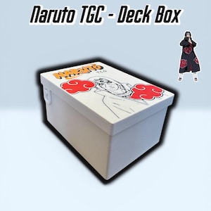 Può includere: Un portamazzo bianco con la scritta "Naruto TCG - Deck Box" in nero. La scatola presenta una grafica di un personaggio con nuvole rosse e la parola "Naruto" in arancione. Un piccolo adesivo del personaggio è a destra.