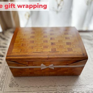 May include: A rectangular wooden box with a woven pattern on the lid and sides. The box is wrapped with a white ribbon tied in a bow. The text "Free gift wrapping" is displayed in a red banner.