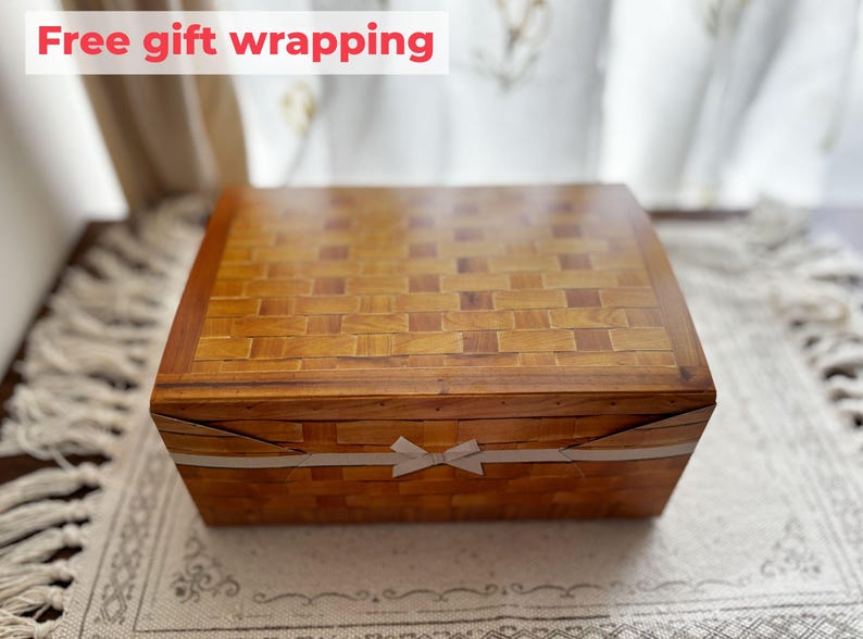 May include: A rectangular wooden box with a woven pattern on the lid and sides. The box is wrapped with a white ribbon tied in a bow. The text "Free gift wrapping" is displayed in a red banner.