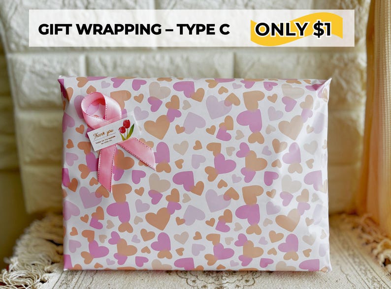 May include: Gift-wrapped package with a heart pattern in shades of pink and peach. A pink ribbon and a small tag with a floral design adorn the package. The text "GIFT WRAPPING - TYPE C" is at the top.