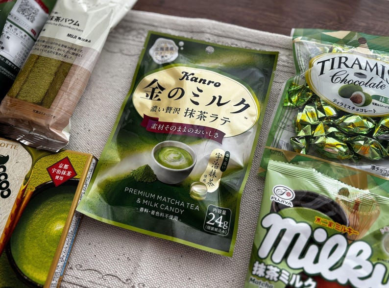 May include: An assortment of Japanese matcha-flavored snacks, including matcha latte candy, tiramisu chocolate, and matcha-flavored biscuits. The packaging features green and gold colors, with Japanese text.