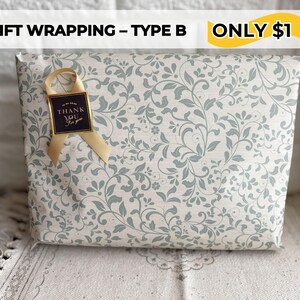 May include: Gift-wrapped package with a floral pattern in light gray and blue. A gold ribbon and a small tag that says "Thank You" are attached. The package is wrapped in decorative paper.