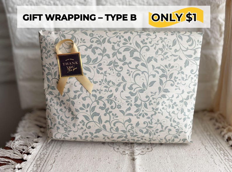 May include: Gift-wrapped package with a floral pattern in light gray and blue. A gold ribbon and a small tag that says "Thank You" are attached. The package is wrapped in decorative paper.