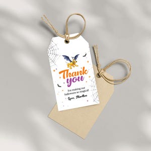 May include: White Halloween-themed gift tag with a cartoon bat and the words "Thank you" in orange and purple. The tag also includes spiderwebs, stars, and the text "For making our halloween so magical! Love, Martten."