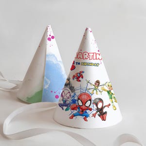 Może przedstawiać: Dwie białe czapeczki urodzinowe z wstążkami. Jedna czapeczka ma akwarelowy wzór z odcieniami niebieskiego i zielonego. Druga czapeczka wyświetla tekst "MARTIN" i "TH BIRTHAY" wraz z kolorowymi ilustracjami Spider-Mana i innych postaci.