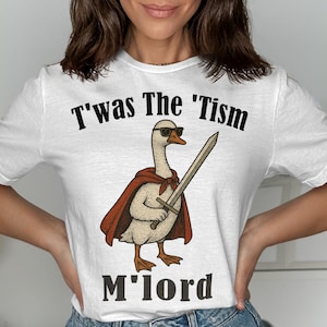 Op de afbeelding: Een wit t-shirt met korte mouwen en een afbeelding van een gans met een zonnebril en een rode cape die een zwaard vasthoudt. De tekst "T'was The 'Tism" staat boven de gans en de tekst "M'lord" is in het zwart onder de afbeelding gedrukt.