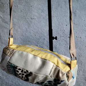 May include: A rectangular crossbody bag with a patchwork design. The bag has a yellow top panel, a cream-coloured central panel, and panels with floral and abstract patterns. It has a beige strap and a zip closure.