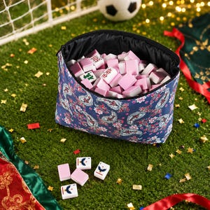 Puede incluir: Un estuche azul marino con cremallera y un colorido estampado de cachemira, lleno de numerosas fichas de mahjong rosas y blancas. Varias fichas de mahjong adicionales con dise&ntilde;os de aves y flores est&aacute;n esparcidas fuera del estuche.