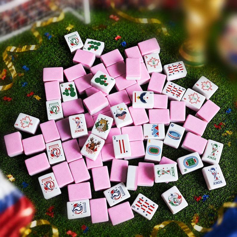 May include: A collection of rectangular mahjong tiles with pink backs and white fronts featuring various colorful illustrations, including soccer-themed graphics, maple leaves, cacti, eagles, and the word JOKER printed on several tiles.