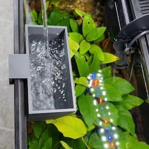 May include: An aquarium with a gray extra-large diffuser, water pouring into it. The tank has green plants, small rocks, and a light strip with red, white, and blue lights. The text "Extra-Large Diffuser" is at the top.
