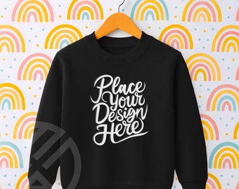 Może przedstawiać: Czarna bluza z napisem "Place Your Design Here" w białym skrypcie. Bluza wisi na drewnianym wieszaku na tle kolorowych tęcz.