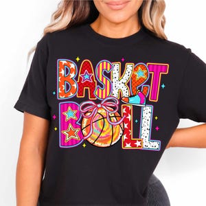 Op de afbeelding: Zwart T-shirt met een kleurrijk grafisch ontwerp met de tekst "BASKETBALL" met een basketbal en een schoen.