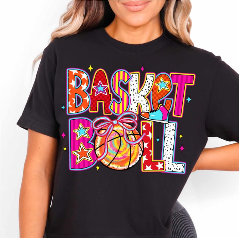 Op de afbeelding: Zwart T-shirt met een kleurrijk grafisch ontwerp met de tekst "BASKETBALL" met een basketbal en een schoen.