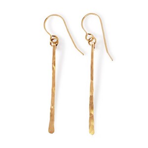 May include: A pair of gold-toned dangle earrings with a hammered, textured finish. The earrings are long and slender, with a simple hook closure.