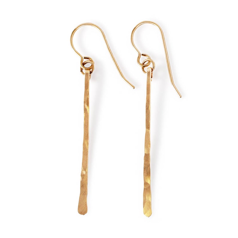 May include: A pair of gold-toned dangle earrings with a hammered, textured finish. The earrings are long and slender, with a simple hook closure.