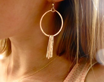 Pode incluir: Brincos de argola dourados com uma corrente pendente de barras de metal martelado.