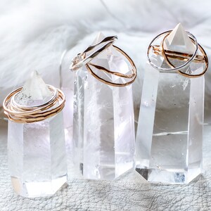 Peut inclure: Trois pointes de cristal de quartz clair avec des anneaux en or et en argent empil&eacute;s sur le dessus. Les cristaux sont sur une surface blanche.