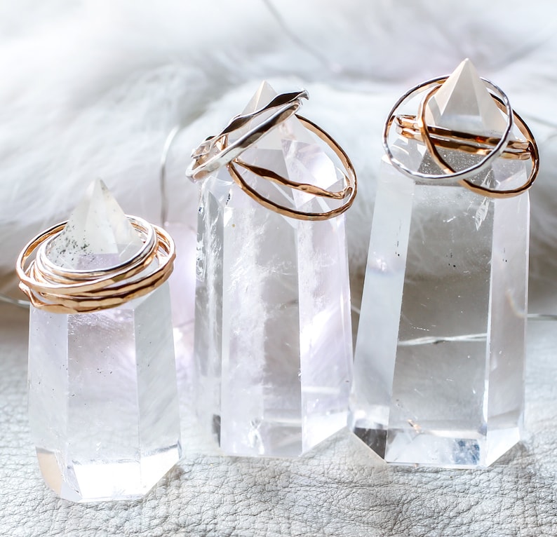 Peut inclure: Trois pointes de cristal de quartz clair avec des anneaux en or et en argent empil&eacute;s sur le dessus. Les cristaux sont sur une surface blanche.