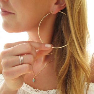 May include: Gold hammered hoop earrings. The earrings are large and circular, with a hammered texture. The earrings are worn by a person with long blonde hair.