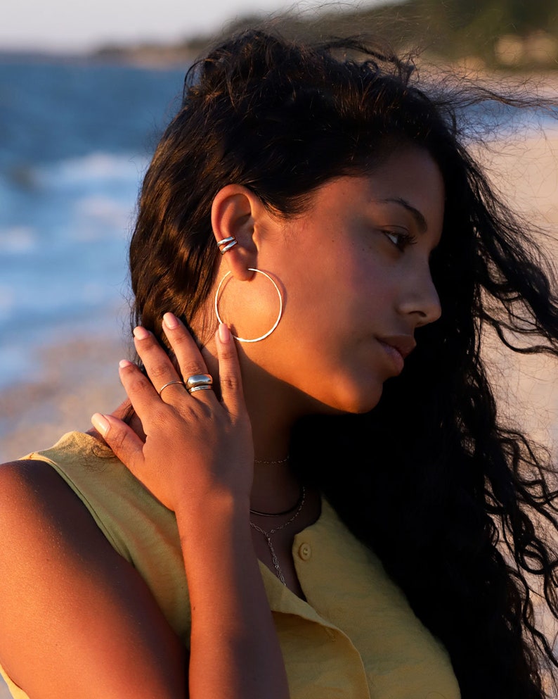 May include: Silver hoop earrings and a silver ring.