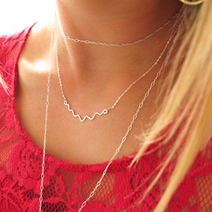 May include: A silver necklace with a wavy design. The necklace is layered over a delicate chain.
